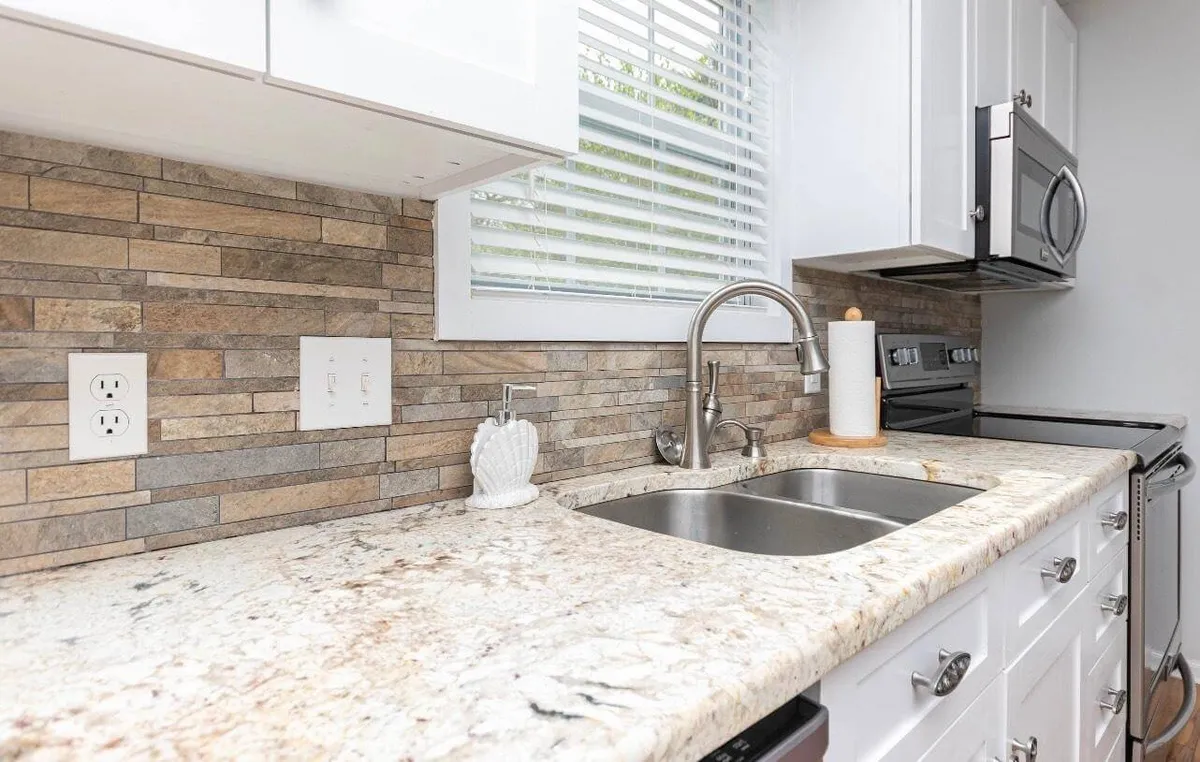 A welcoming kitchen with gleaming granite countertops, a modern sink, stylish backsplash, and stainless steel appliances. The space is set up for cooking and entertaining, inviting guests to gather and enjoy meals together.