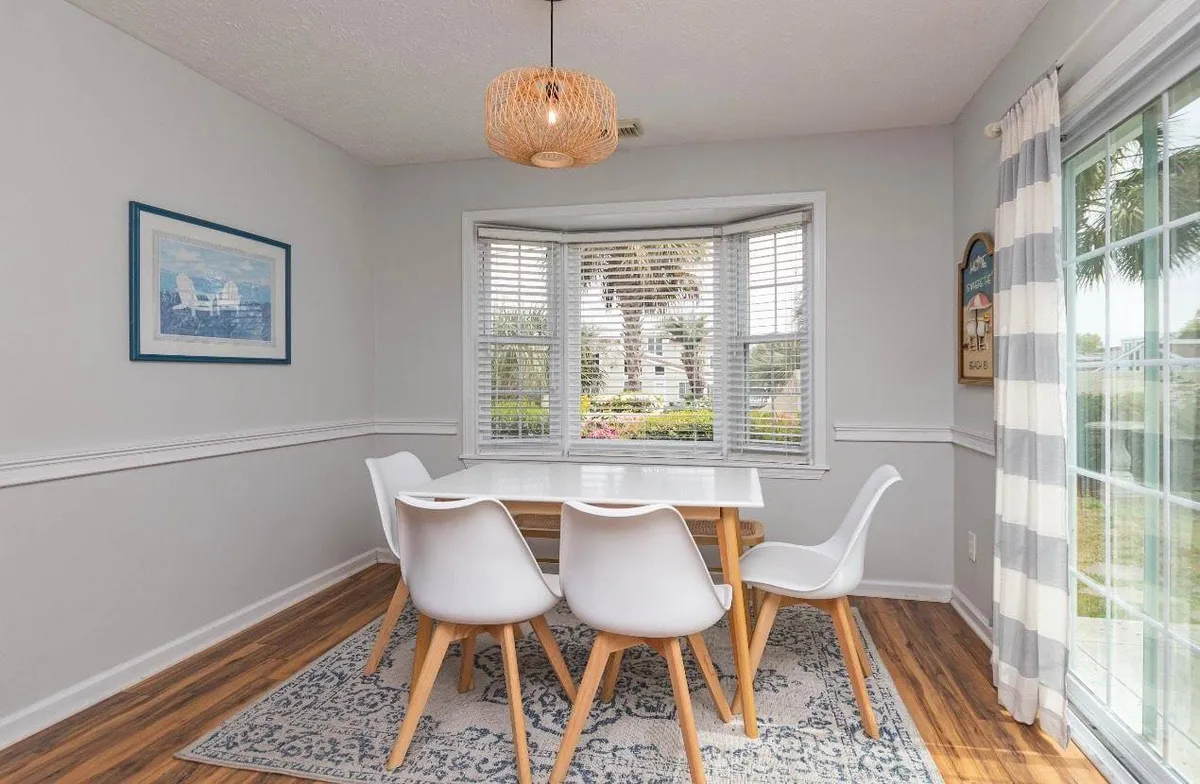 This image displays a light-filled dining area with a sturdy dining table, comfortable chairs, a window letting in the morning sun, and an elegant light fixture. The setting is perfect for family meals, intimate gatherings, or laughter-filled dinners.