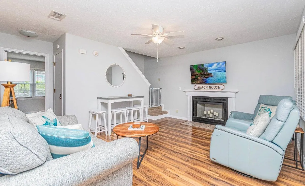 This interior shot reveals a cozy, open living and dining area with a comfortable couch, a dining table, a fireplace, and a TV with a beach scene. The setup is designed for both lounging and sharing meals, seamlessly merging relaxation with togetherness.