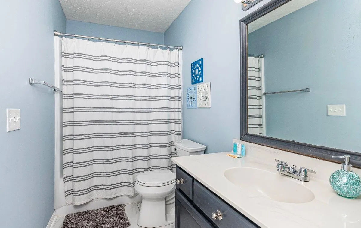 A full bathroom featuring a vanity with a sink, a large mirror, a shower with a curtain, toilet, and decorative wall art. The space is bright, organized, and inviting, ideal for personal grooming and post-beach refreshment.